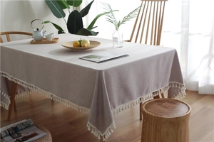 Detail of solid color linen-textured tablecloth with white fringe tassels on wooden table