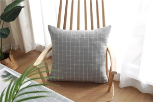 Close-up of grey plaid cushion with fringe on a wooden chair in a bright living room