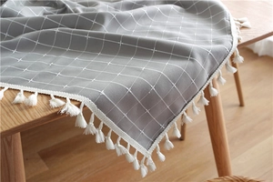 Detail of grey plaid tablecloth with white tassels on a light wood dining table
