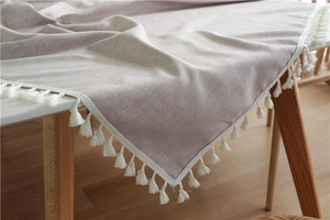 Detailed view of beige linen tablecloth featuring white decorative fringe tassels on wood table