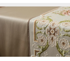Detailed close-up of champagne satin table runner with elegant floral embroidery and texture
