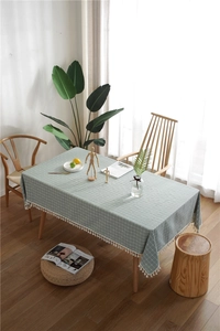 Detail of grey-green plaid tablecloth featuring white tassel fringe on a wooden table