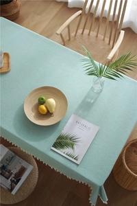 Close-up of light green linen tablecloth featuring elegant white tassel fringe details