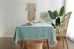 Close-up of mint green linen-textured tablecloth with white tassel edges and minimalist style