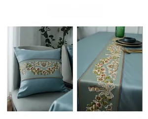 Detail of light blue satin table runner and cushion with floral embroidery and gold piping