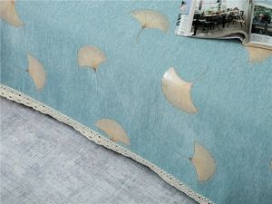 Detailed texture of blue chenille sofa cover with golden ginkgo leaf pattern and lace edge