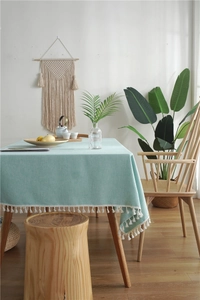 Close-up of mint green linen tablecloth with white cotton tassel fringe detail on a wood table