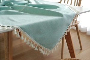 Close-up of mint green linen tablecloth with elegant white fringe trim on a wood table