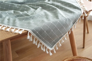 Detail of grey-green plaid tablecloth with white tassels on a wooden table surface