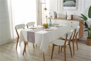 Detailed view of cream linen tablecloth with fringed edges and dark textured table runner