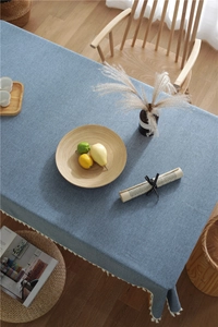 Close-up of blue linen fabric tablecloth with white tassel fringe on wooden table