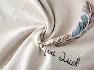 Detailed close-up of thick beige chenille sofa cover with embroidered feather and good luck text