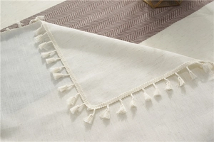 Close-up of beige linen table runner showing delicate textures and handmade tassel edges