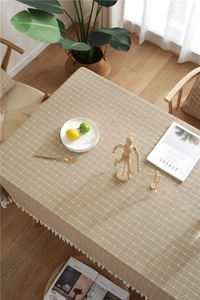 Detail of light khaki checkered tablecloth with fringe edges on a wooden table
