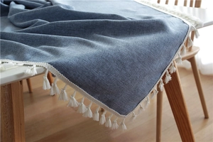 Detail of greyish blue woven tablecloth featuring elegant white tassel fringe borders