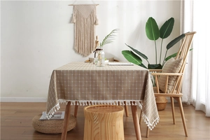 Detail of khaki checkered tablecloth featuring white tassel fringe on a wooden table