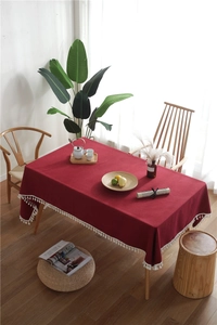 Detail of dark red rectangular tablecloth with white tassel edges and heavy linen texture