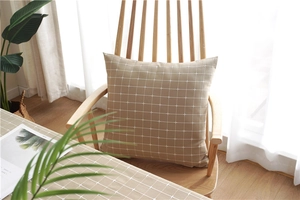 Detail of warm khaki checkered pillow on a wooden chair with matching tablecloth