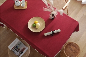 Detail of wine red rectangle tablecloth with white pom pom tassels and linen texture