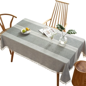 Gray striped linen table runner with white crochet lace and tassel trim on wooden table