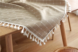 Macro detail of beige grid tablecloth with decorative white fringe on wooden table