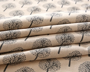 Close-up of linen fabric showing texture and black tree prints on a beige tablecloth