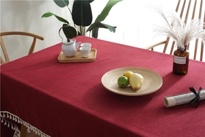 Detail of dark red linen tablecloth featuring white tassel fringe on a wooden dining table