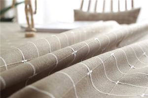 Close-up detail of light brown jacquard tablecloth with textured white grid embroidery