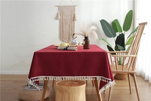 Detail of dark red linen tablecloth with white tassel trim in a Nordic home setting