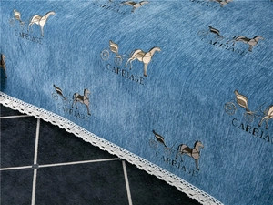 Detail of blue chenille fabric featuring vintage carriage pattern and white lace trim