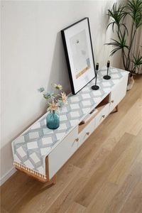 Close-up of geometric chenille table runner with white fringe tassels on a TV cabinet