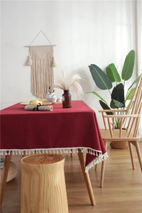 Close-up of deep red linen-textured tablecloth with elegant white fringe tassel edges