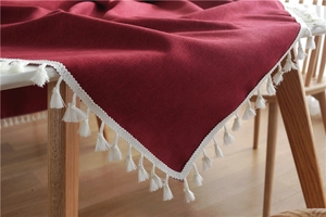 Close-up of deep red linen tablecloth with elegant white cotton tassel fringe detail