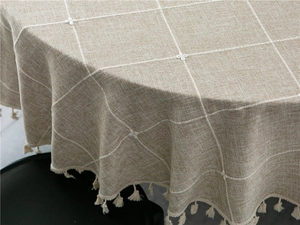 Detail of minimalist beige plaid tablecloth with embroidered flowers and cotton tassels
