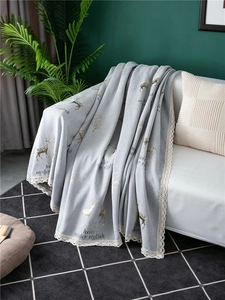 Detail of gray chenille sofa cover with deer embroidery and delicate white lace trim