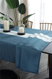 Detail of teal waterproof tablecloth with white center stripe and black text on wooden table