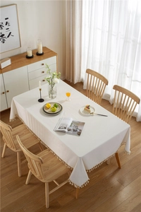 Close-up of cream white thick tablecloth with decorative tassel edges on a wood table