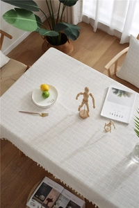 Detail of beige plaid tablecloth featuring elegant tassel edges on a wooden table