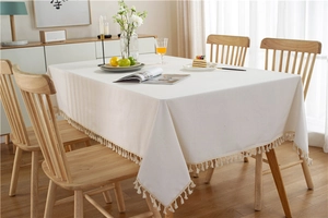 Detailed close-up of cream white tablecloth with fringe edges and pompom decor on wood table