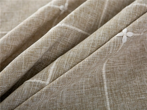 Close-up of light brown plaid tablecloth with delicate white floral embroidery texture