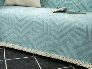 Detail of teal chenille sofa cover with geometric leaf patterns and white lace trim
