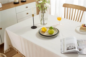 Close-up of white tablecloth with beige tassel fringe on a wooden dining table