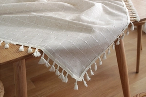Close-up of beige jacquard tablecloth featuring white cross patterns and tassel fringe edge