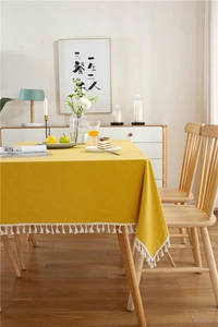 Detailansicht der gelben Baumwolltischdecke mit weißen Quasten auf dem Holztisch