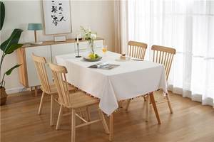 Close-up of thick white tablecloth featuring colorful pom-pom fringe on a wooden table