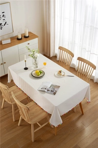 Close-up of modern white tablecloth with colorful pom-pom fringe on a wooden table