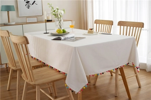 Detail of white rectangle tablecloth with colorful pom-pom fringe in a modern dining room