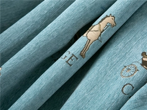 Close-up of thick light blue chenille fabric with golden carriage pattern embroidery