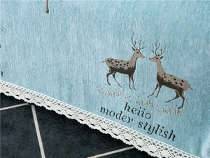 Detail of light blue chenille sofa cover with deer pattern and white lace edge