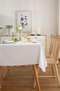 Detail of white linen tablecloth featuring colorful pompom fringe for modern dining rooms